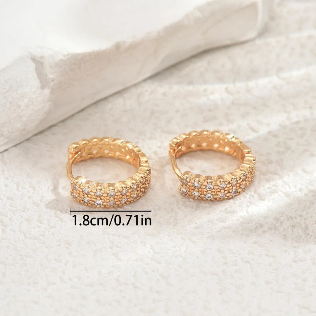 Close-up of geometric copper ear studs showing a ring with a central dot, on a plain background.