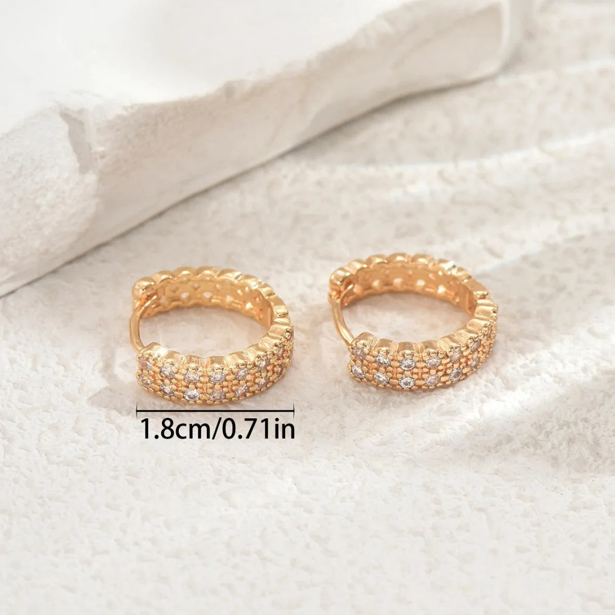 Close-up of geometric copper ear studs showing a ring with a central dot, on a plain background.