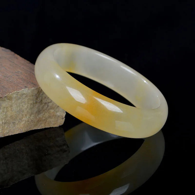 A polished light jade bracelet in a classic Chinese style band design on a plain background.