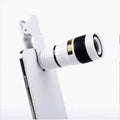 Black 12X smartphone telephoto lens with adjustable mounting clip and cleaning cloth on a table.