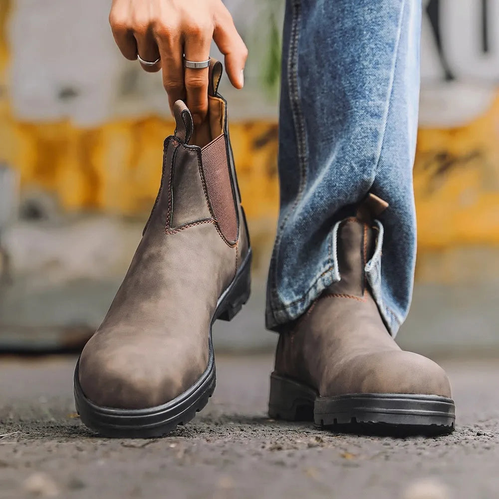 Vintage brown unisex Chelsea boot with frosted PU upper and car suture detailing on a wooden floor.
