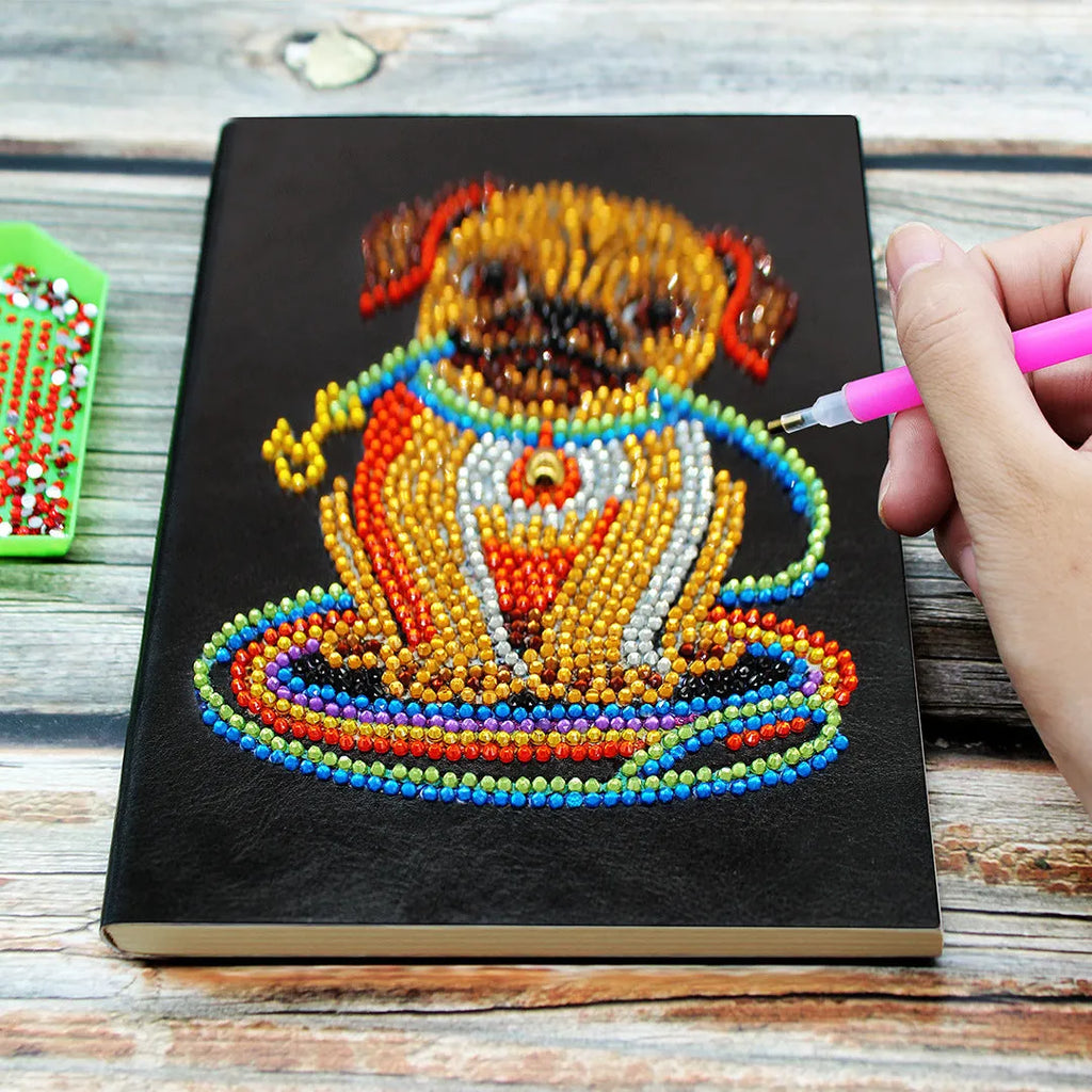 Black A5 hardcover diamond painting notebook with elastic closure, shown closed and open on a crafting table.