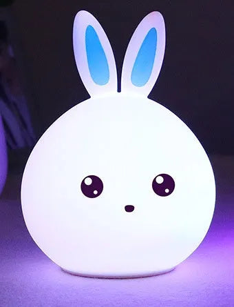 Cute rabbit-shaped night light made of soft silicone with touch sensor, showing seven LED colour options, on a bedside table.