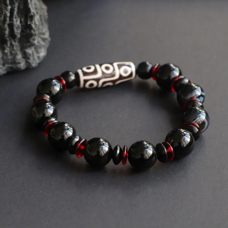 Hand-woven black agate dzi bead bracelet with geometric chalcedony beads on a wrist.