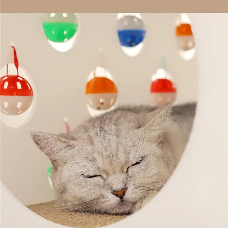 White plastic house-shaped cat scratch board with sisal siding, an arched tunnel entrance, and a dangling red bell ball toy.