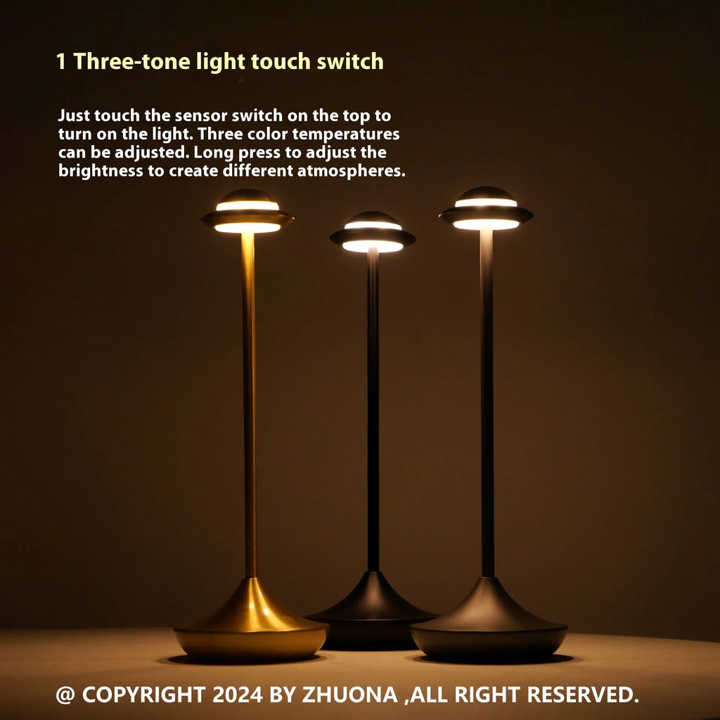 Modern metallic UFO-shaped table lamp with touch base in black, on a wooden desk.