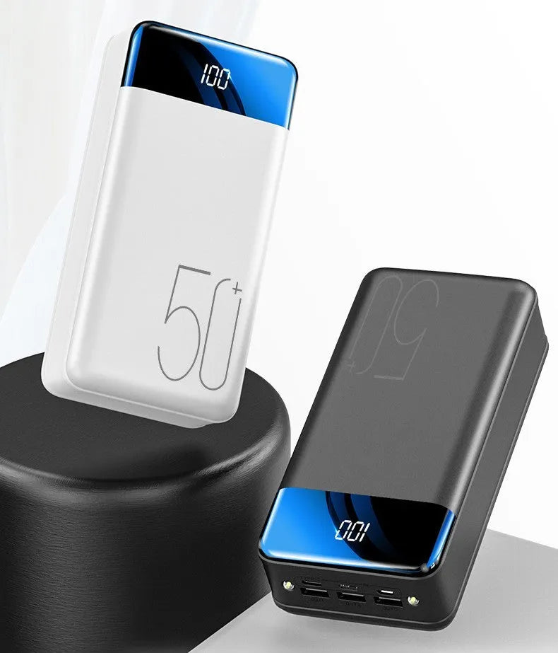 Black and white large 50000mAh portable power bank with multiple USB ports, showing scale next to a smartphone.