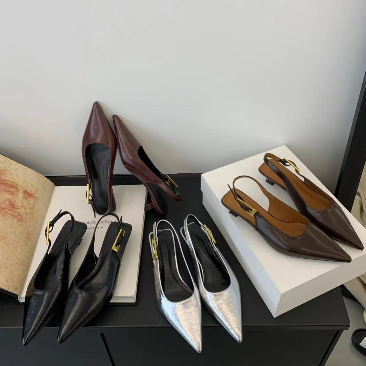 Women's black pointed toe leather shoes with a thin low heel and ankle strap on a rubber sole.