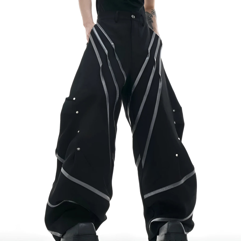 Men's black trousers with pleated detail and metal rivets, showing three-dimensional cut.