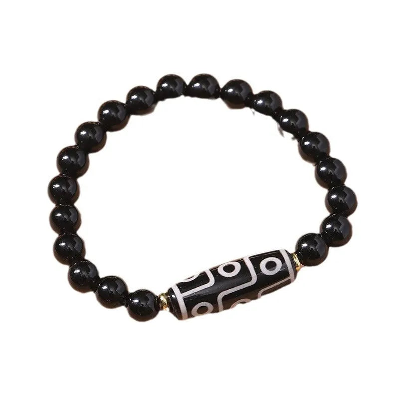 Close-up of a black obsidian dzi bead agate bracelet with adjustable cord, showing ethnic Tibetan design.