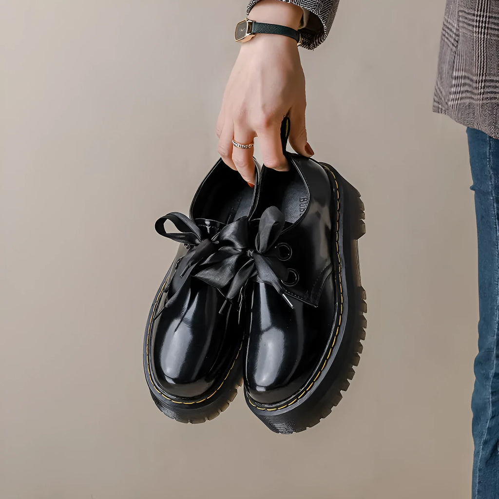 Women's black leather shoes with a thick sole, cross straps, and ribbon laces laid flat.
