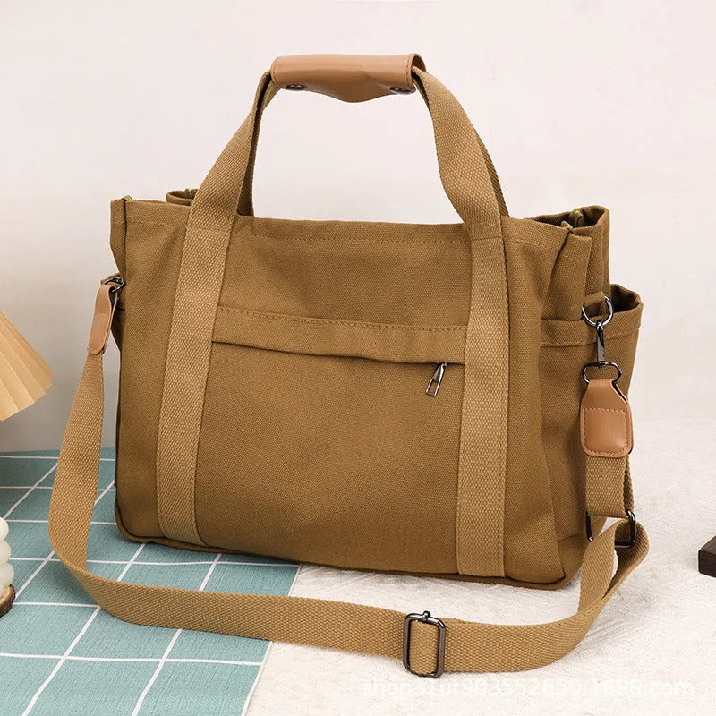 A horizontal square canvas tote bag in army green with a cross-body strap and visible sewing lines.