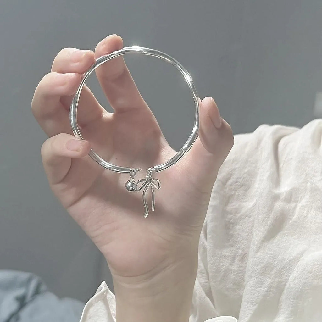 Silver adjustable bracelet with a detailed opening bow charm on a model's wrist, showing the lobster clasp.