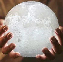 3D printed white moon lamp on a wooden holder, showing detailed lunar surface and a glowing yellow light.