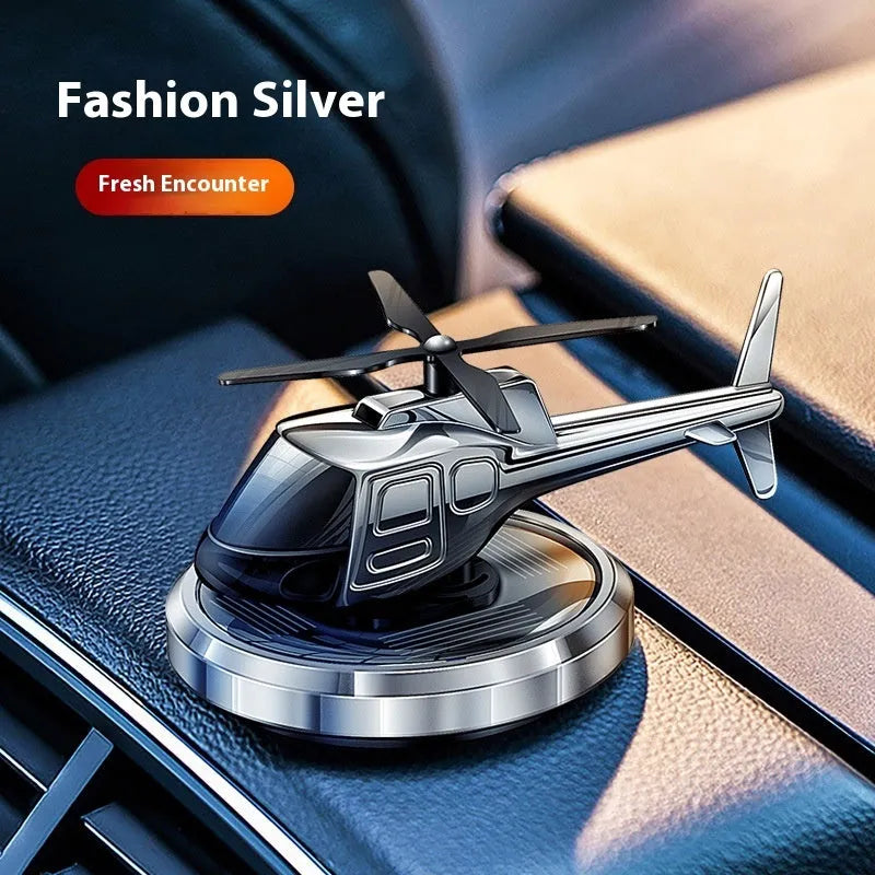 Silver metal solar-powered helicopter car air freshener rotating on a dashboard