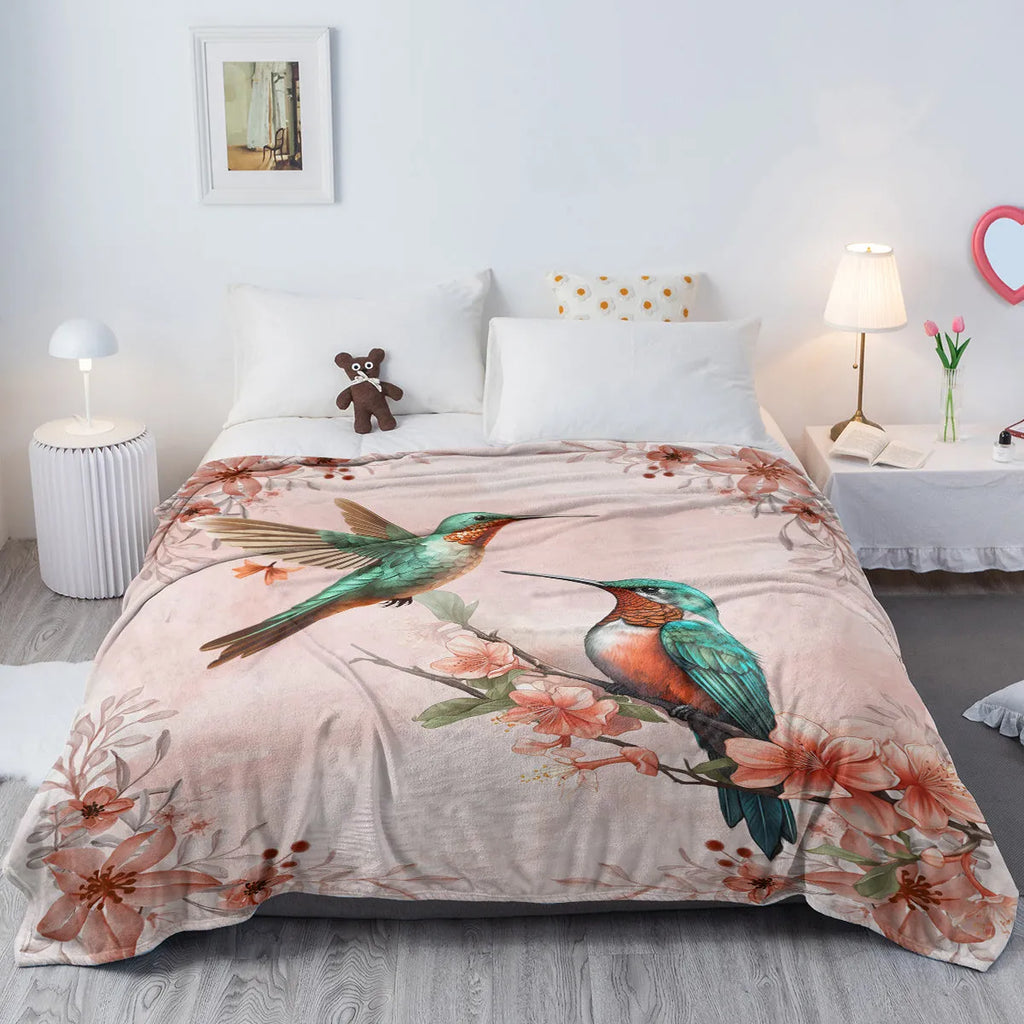 Pink hummingbird floral fleece throw blanket made of soft flannel velvet, folded on a sofa