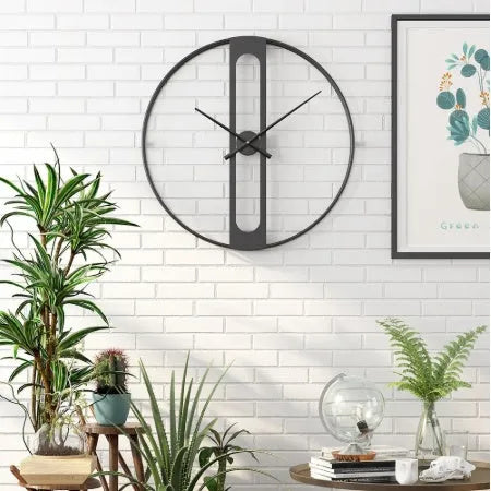 Large round metal wall clock with Roman numerals on a white wall.