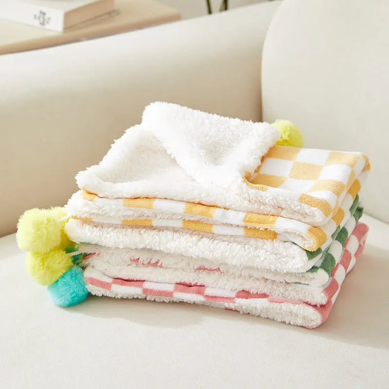 Green plaid pattern fleece pet blanket with a fur ball decoration, shown on a sofa.