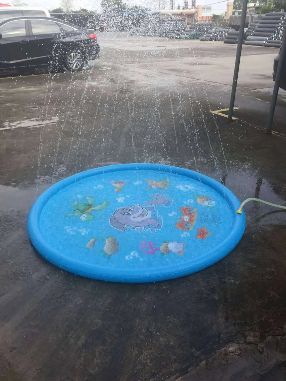Blue children's water spray play mat with marine animal graphics on grass connected to a hose