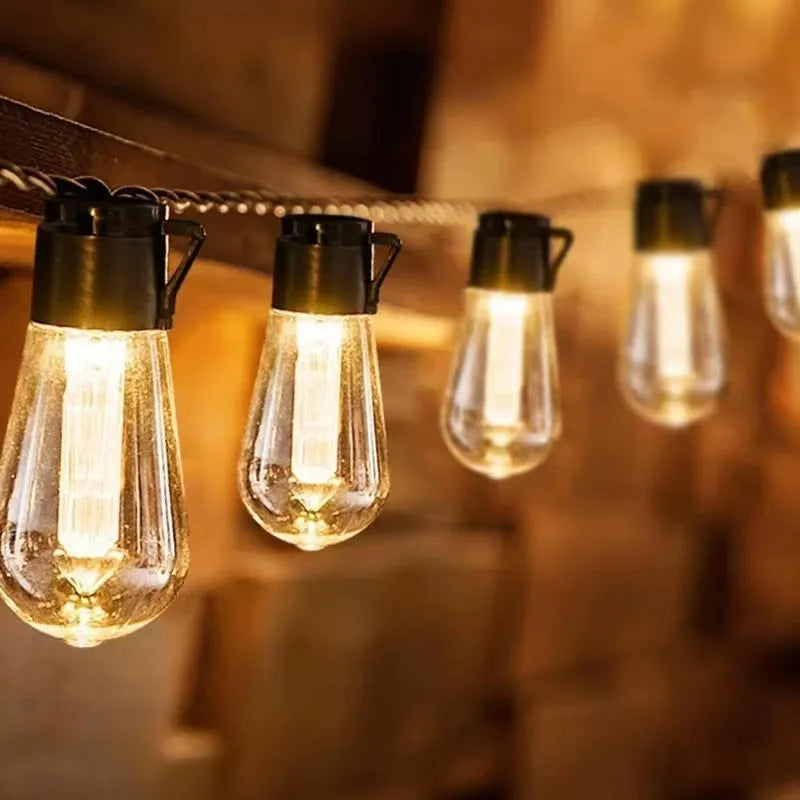 Outdoor retro long bulb infusion bottle shape string lights hanging in a garden setting.