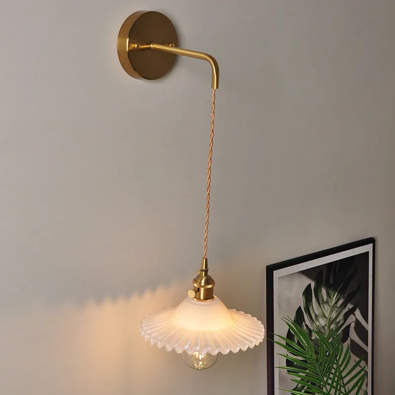 Retro brass lotus wall lamp with glass shade mounted on a beige wall, showcasing its copper arm and layered design.