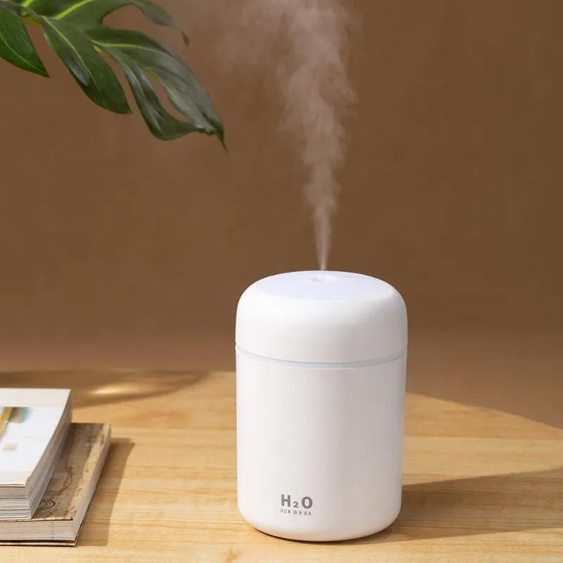Pink USB desktop humidifier with coloured LED lights and water tank on a wooden desk.