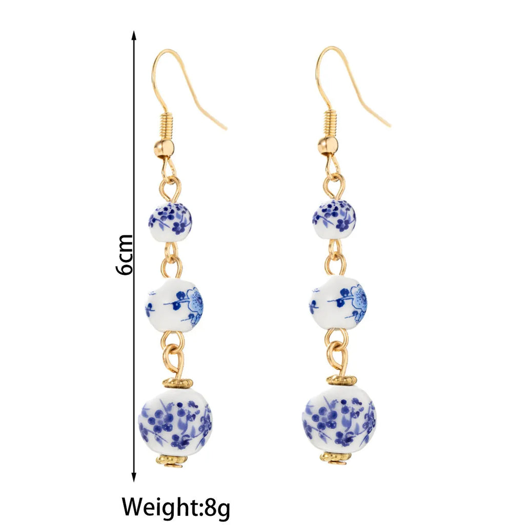 Long blue and white porcelain ceramic bead earrings with geometric alloy details on a white background.