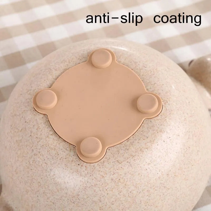 Three wheat straw dinosaur bowls in pink, green, and beige on a kitchen table