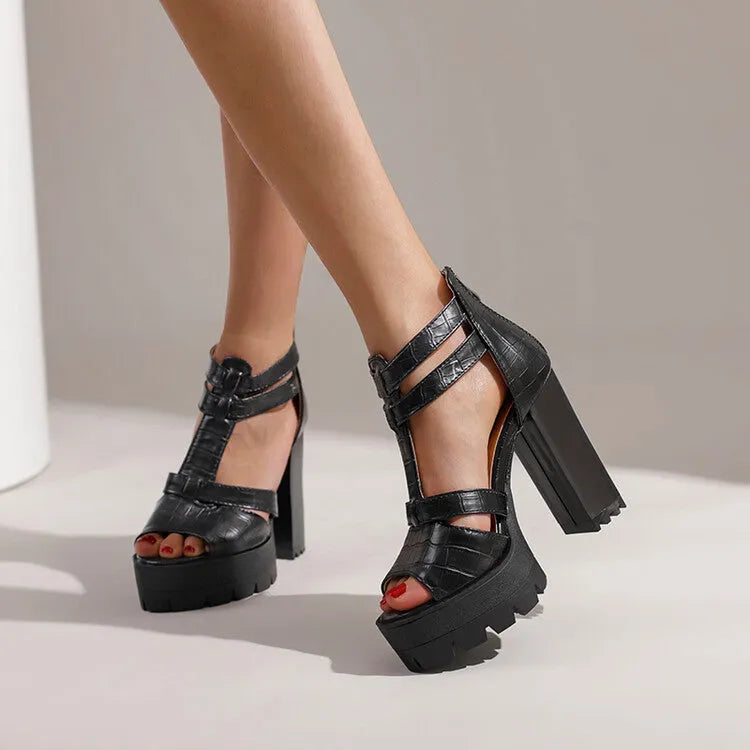Black platform high heel sandals with a round toe and back zipper on a wooden floor.