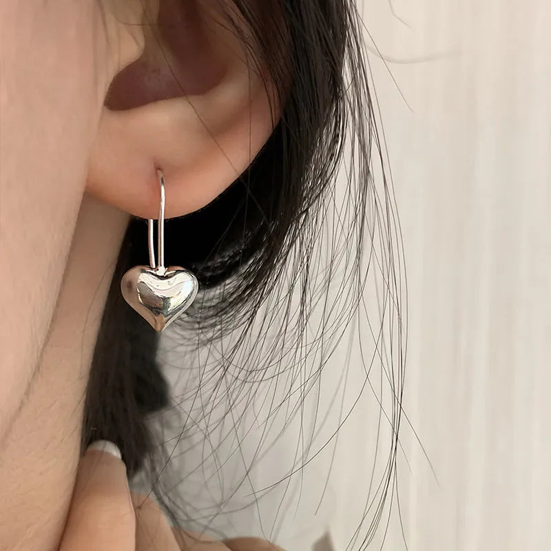 Silver coloured heart-shaped earrings with a glossy three-dimensional design on a white background.