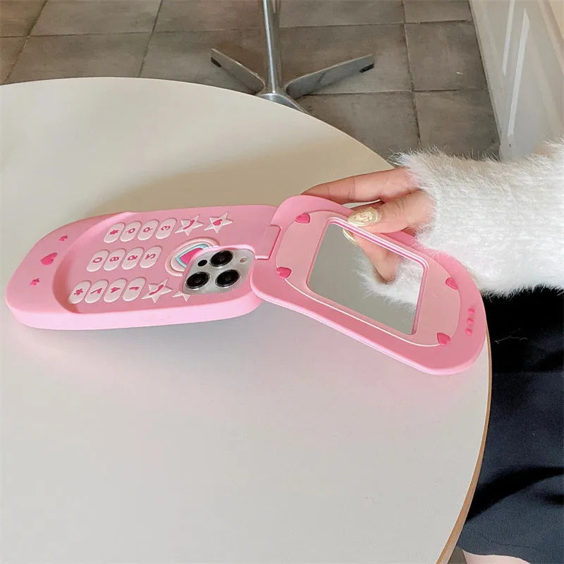 Light pink silicone flip phone case with a pop-out mirror and a cartoon charm, shown next to an iPhone.