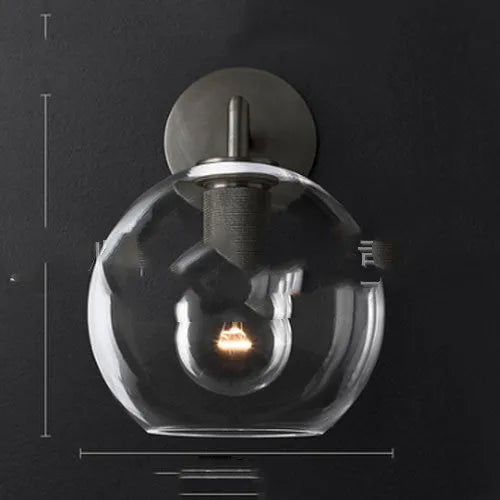 Gold bronze or black wall lamp with triangular transparent glass shade and wrought iron frame for bedside or hallway use
