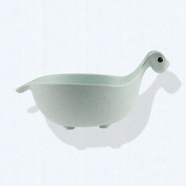 Three wheat straw dinosaur bowls in pink, green, and beige on a kitchen table