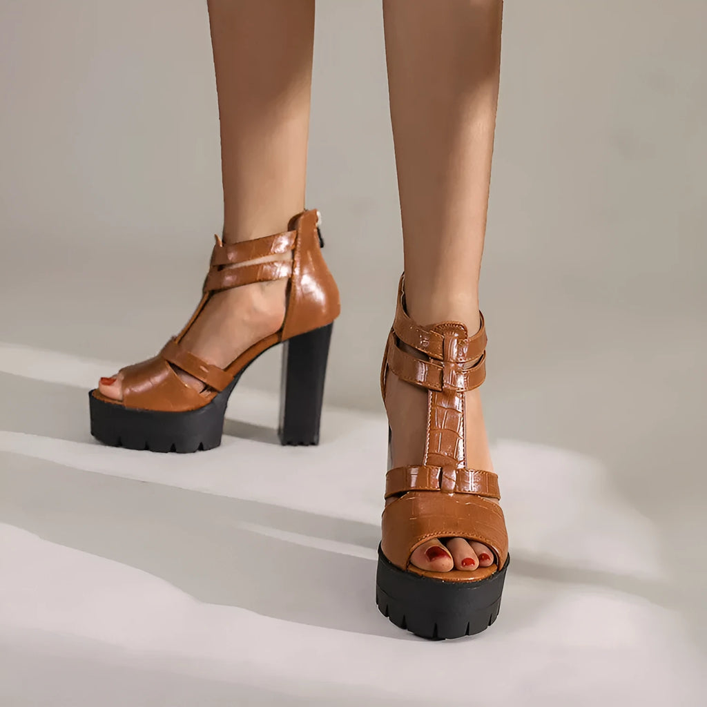 Black platform high heel sandals with a round toe and back zipper on a wooden floor.