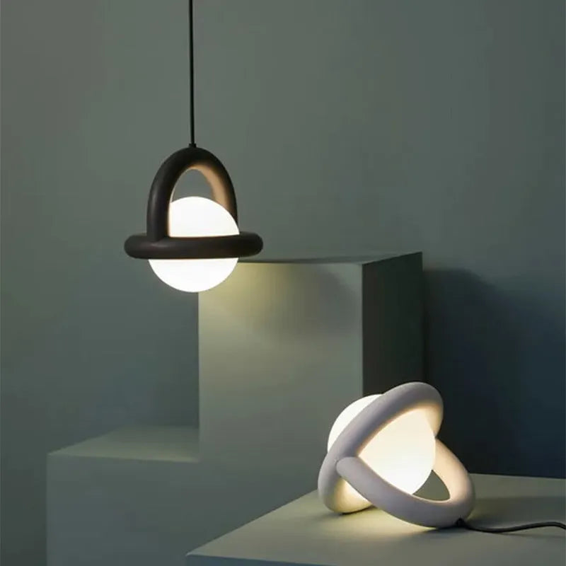 Matte black hanging line lamp with a long black cord suspended above a bedside table.