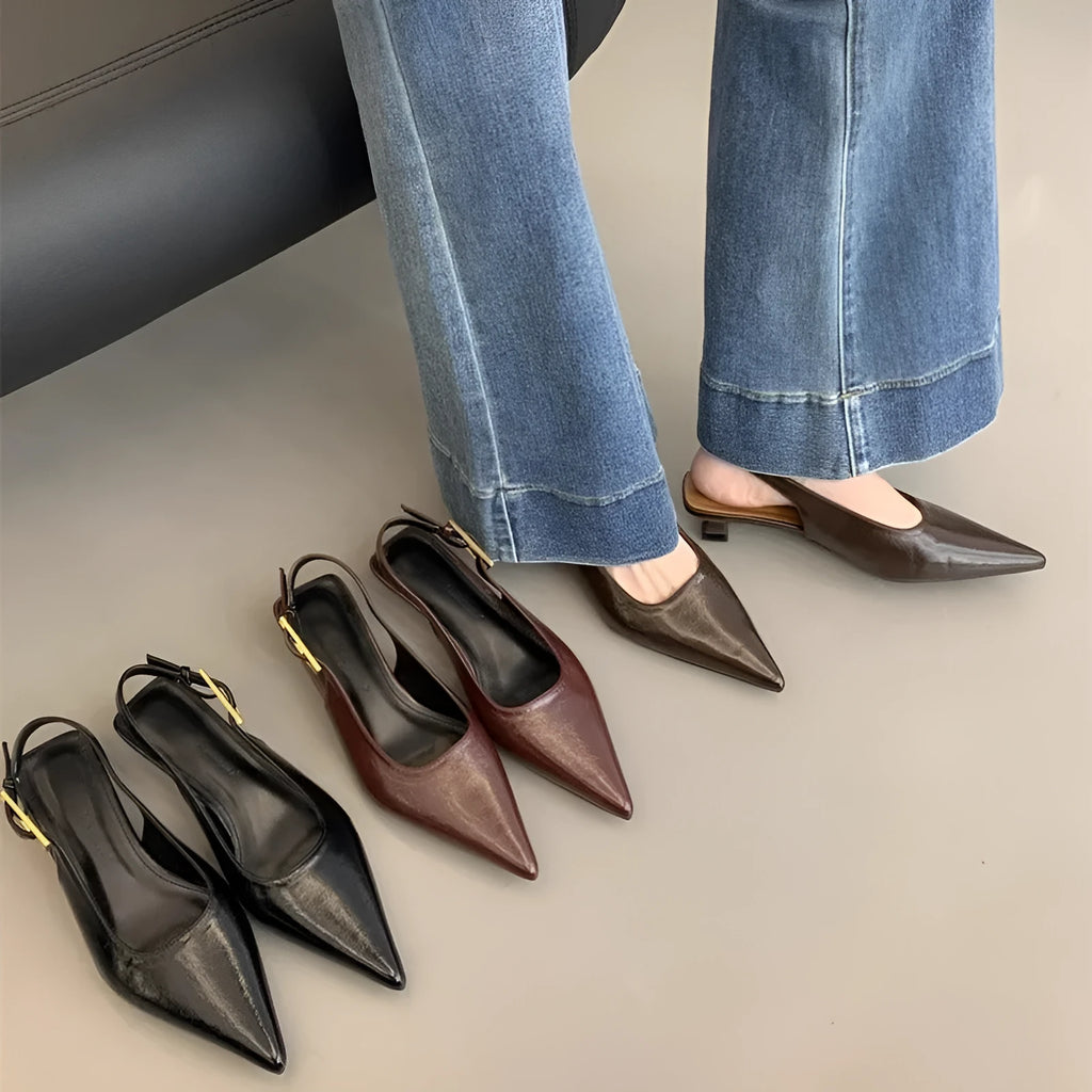 Women's black pointed toe leather shoes with a thin low heel and ankle strap on a rubber sole.