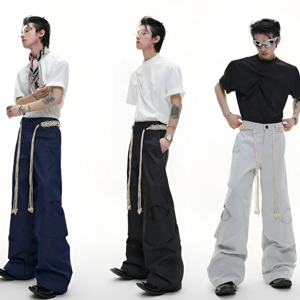 Man wearing dark blue cotton straight-leg trousers with heavy 3D belt stitching and decorative tassel details.