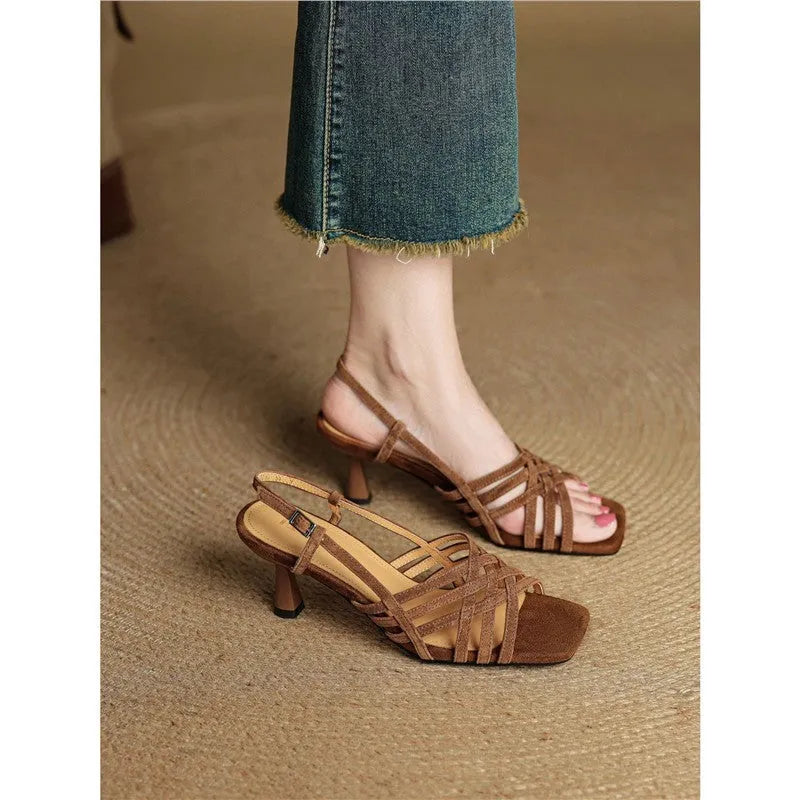 Light brown women's sandals with thin cross-straps, an ankle buckle, and a 3-6cm mid heel on a wooden floor.