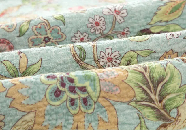 Blue American-style floral and bird quilted cotton bedspread set on a bed, showing textured stitching.