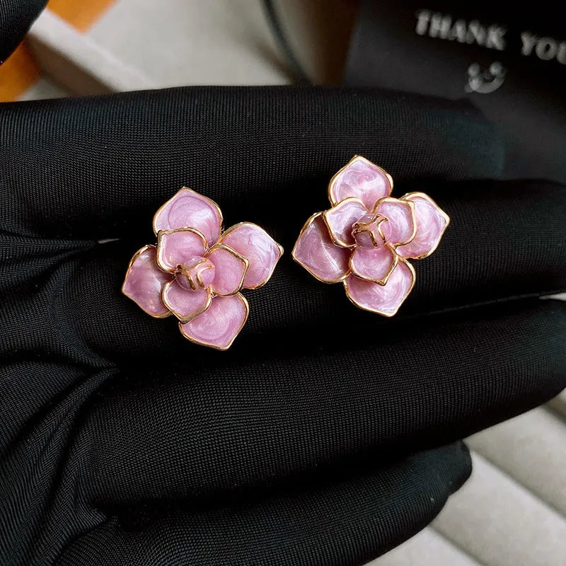 Close-up of gold plated purple flower stud earrings with iridescent oil-spot glaze on a copper base.