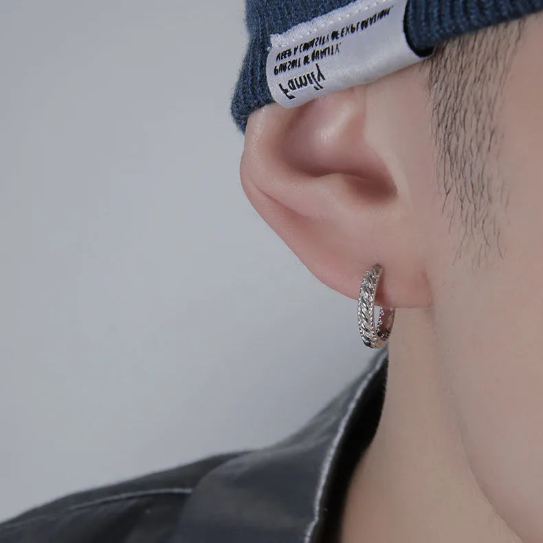 Close-up of a pair of men's geometric copper hip hop earrings on a dark background.