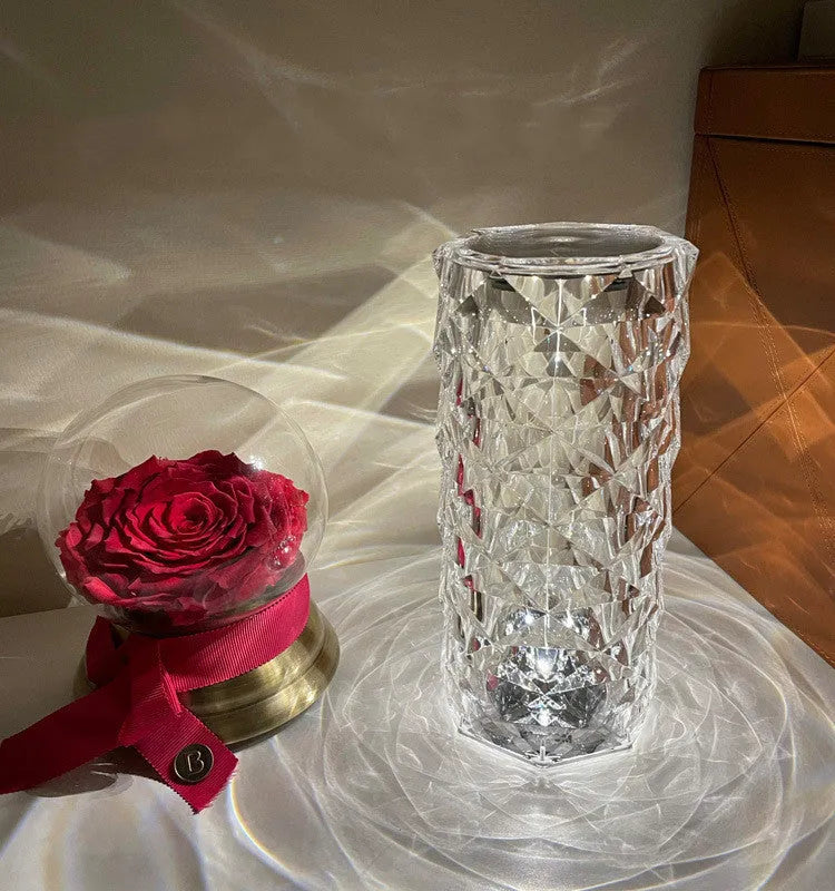 Clear acrylic crystal rose shaped LED table lamp with diamond-like facets on a table.