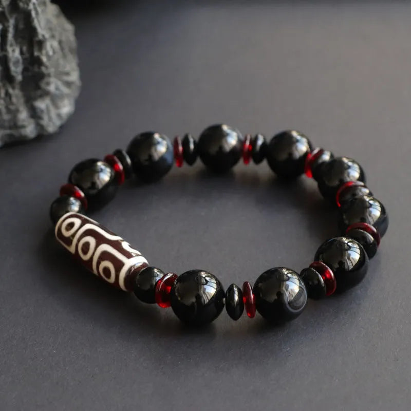 Hand-woven black agate dzi bead bracelet with geometric chalcedony beads on a wrist.