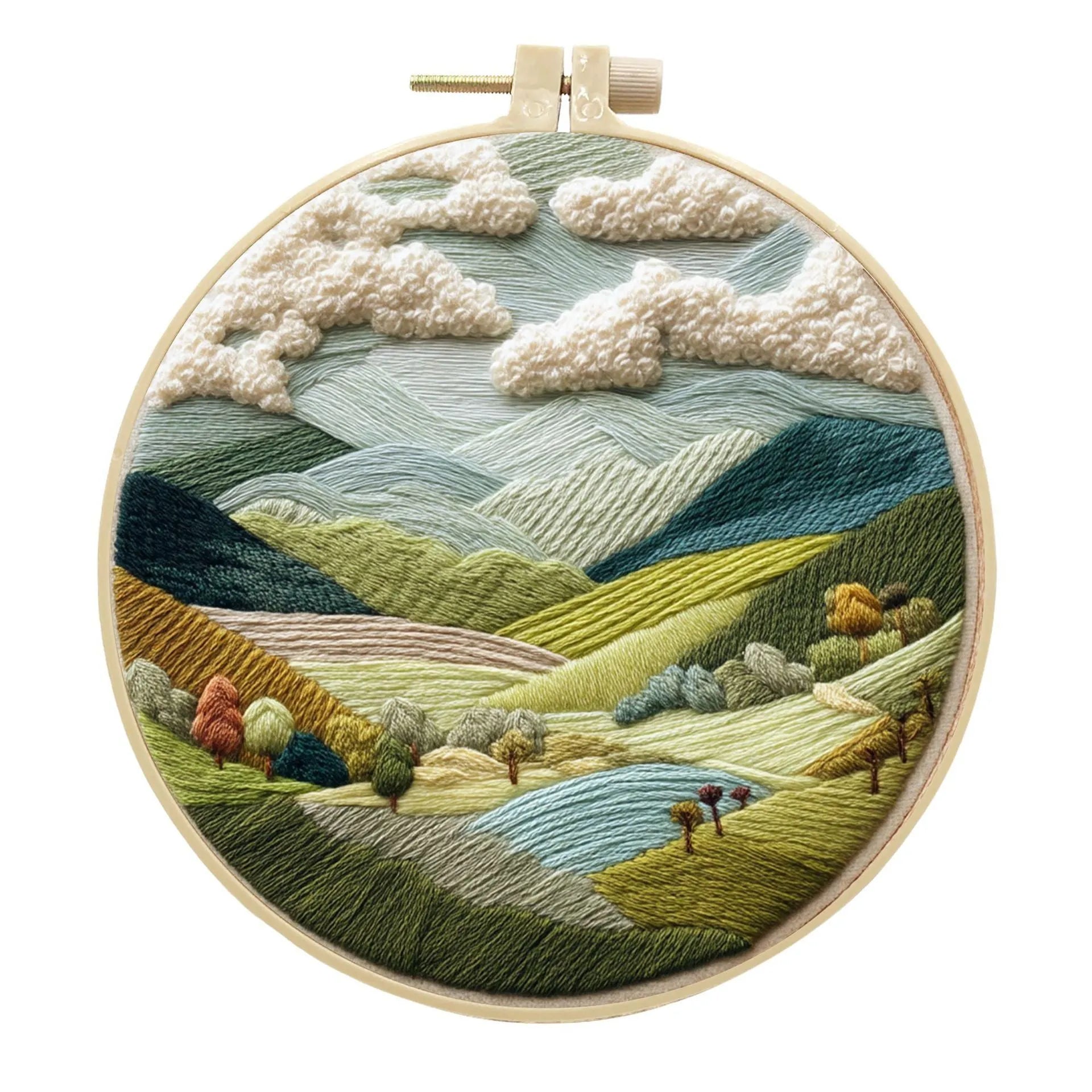 Embroidery DIY kit components: printed landscape fabric, embroidery hoop, coloured threads, and needles laid flat.