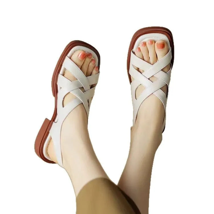 Women's black patent leather square toe sandals with a cross strap and low heel on a white background.
