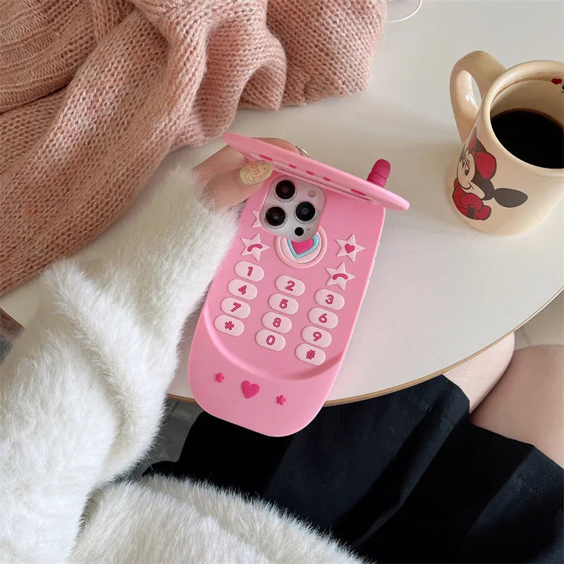 Light pink silicone flip phone case with a pop-out mirror and a cartoon charm, shown next to an iPhone.