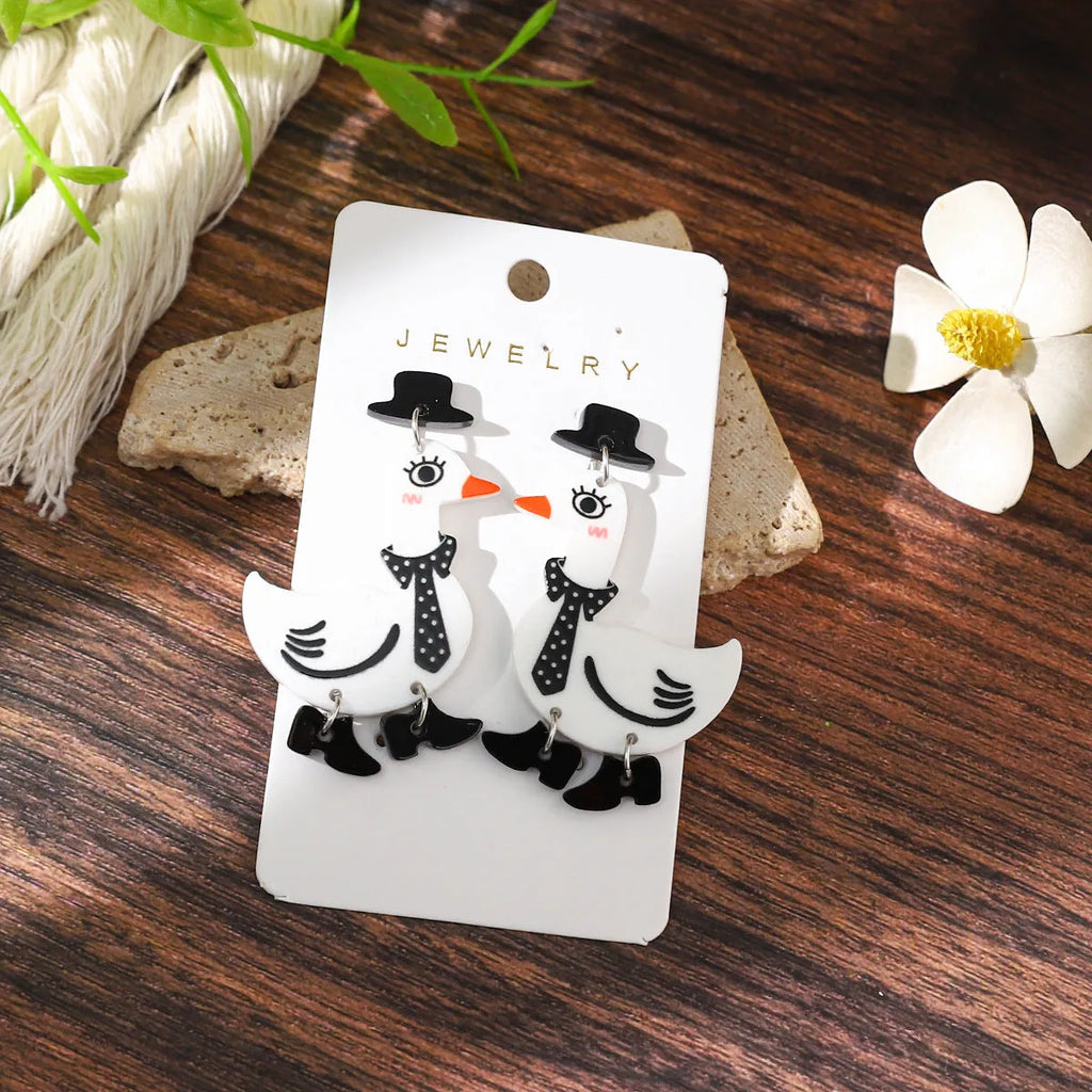 Three pairs of acrylic cartoon duck earrings in pink, white, and yellow on a light background