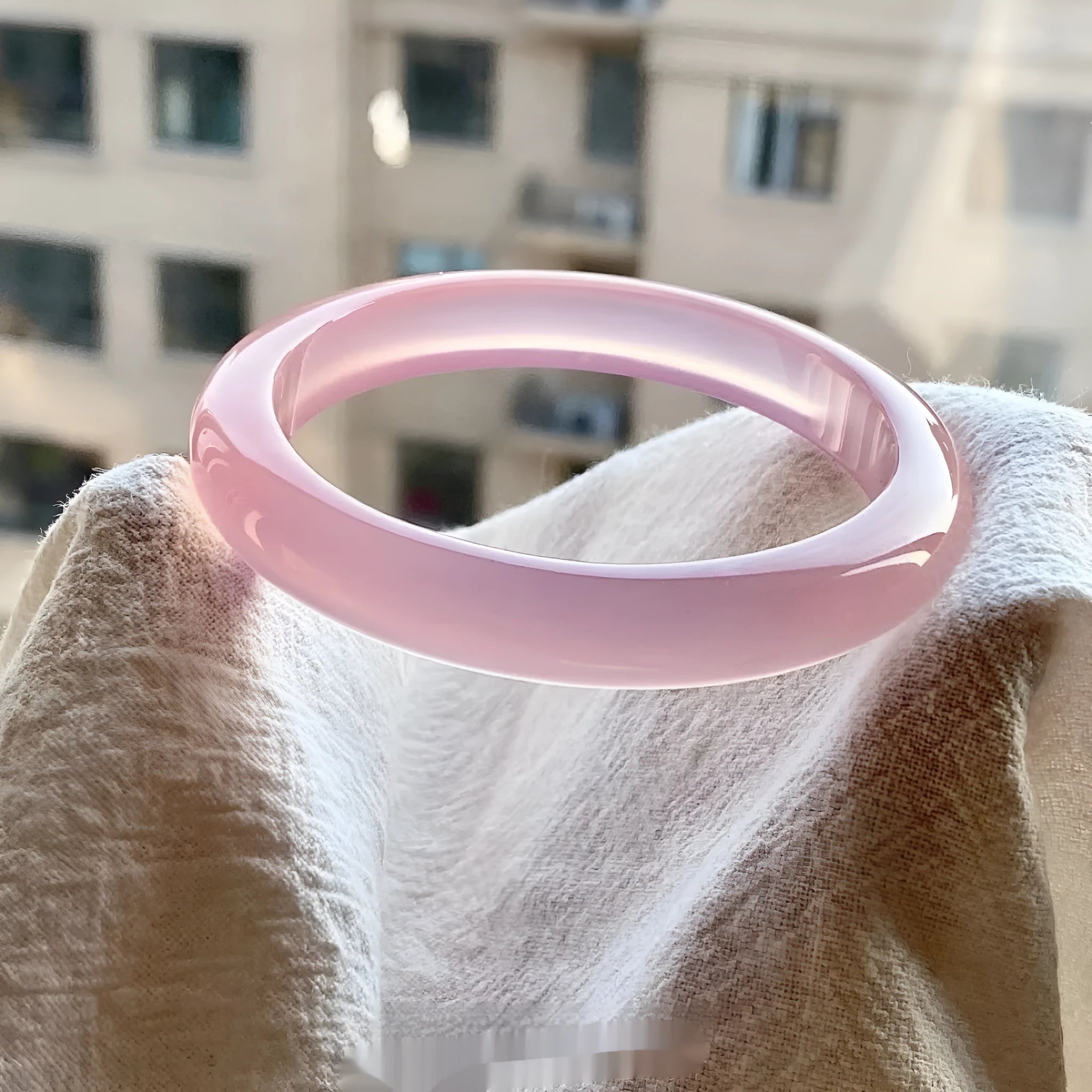Natural agate wide tire bracelet in pink on a wrist, showing polished bead design.