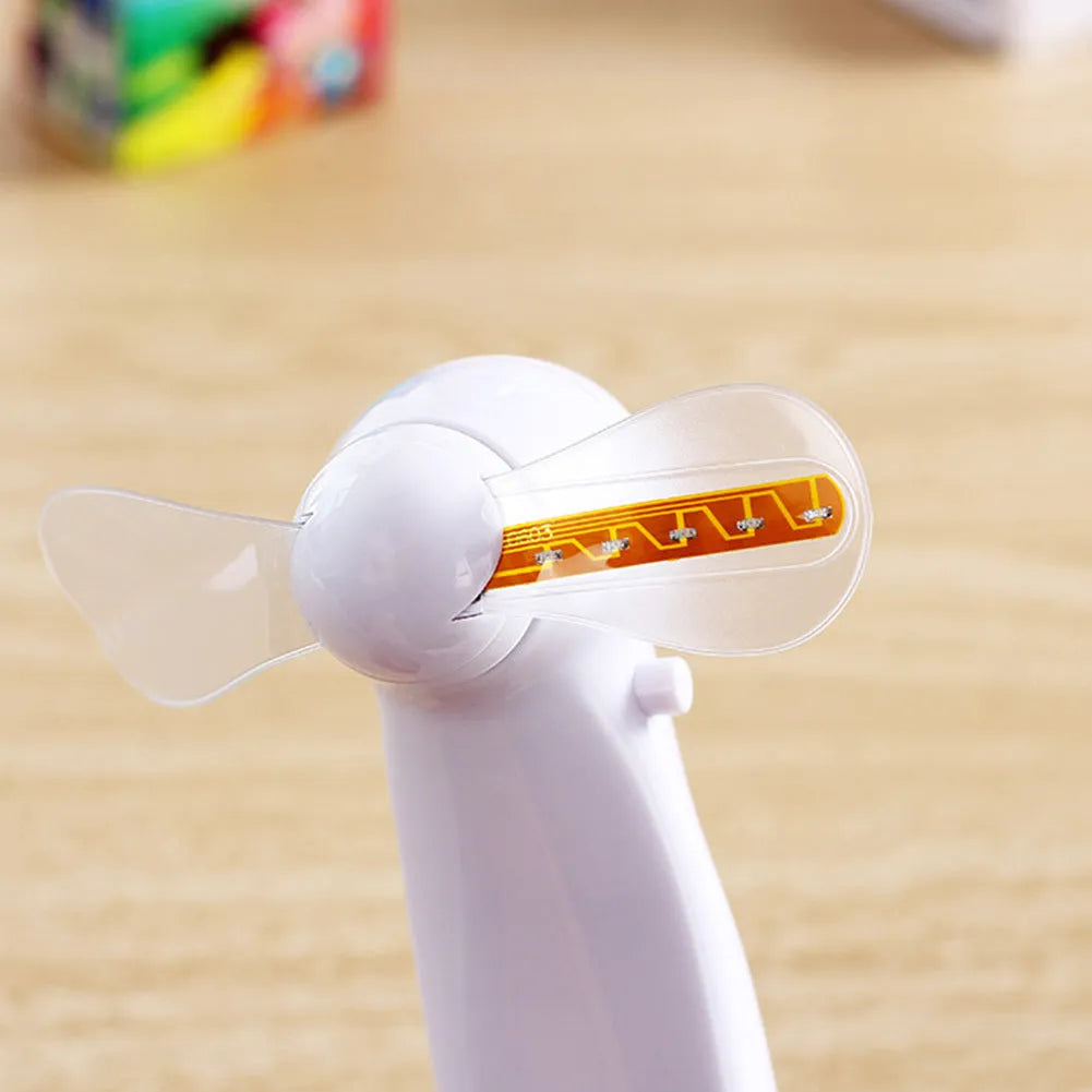 White handheld mini fan with LED lights displaying a love heart pattern, shown next to AAA batteries for scale.