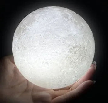 3D printed white moon lamp on a wooden holder, showing detailed lunar surface and a glowing yellow light.
